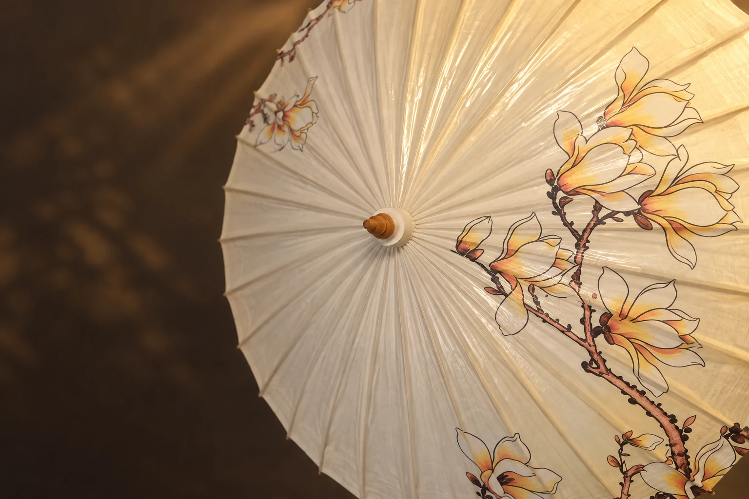 Magnolia artwork and the wooden crown of a SHENGHE umbrella, shown in a reference-based editorial image.
